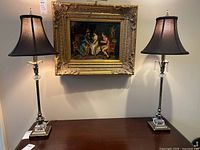 Pair of matching table lamps placed on a wooden table beneath a painting, showing both lamps fully including bases and shades