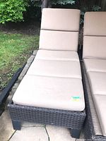 Full view of the rattan style lounger chair with beige cushioned upholstery outdoors on patio.