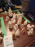 Overview photo showing 19 cast resin Netsuke figures arranged on a table, made of white resin, depicting various characters and a small pagoda structure