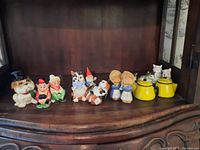 Full view of all ceramic figurines and salt and pepper shakers arranged on a wooden shelf.
