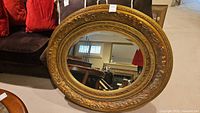 Front and angled views of the wood framed oval mirror showing detailed ornate gold-tone carved frame and oval glass.