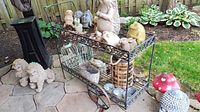 Side angled view of the black metal patio garden cart on a stone tiled patio with various garden statues and decorative items placed inside and around it.