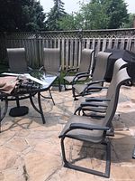 Six patio chairs arranged around glass table on stone patio