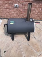 View of whole pizza oven showing its curved black metal body, handles on sides, and short legs for stability.