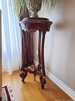 Full view of the tall round wooden plant stand with green marble top, curved legs and metal accents