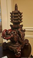 Front angled view of dark plaster elephant sculpture with multi-tier pagoda on back showing details and wear.