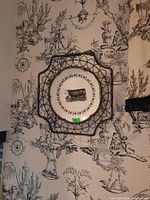 Full view of the ceramic plate in wire frame holder against patterned wallpaper.
