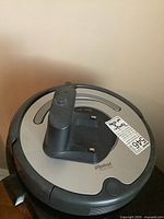 Top angled view of the iRobot Roomba robotic vacuum cleaner showing the raised sensor/charging module and iRobot branding.