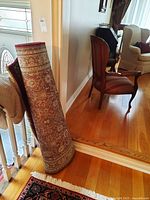 Runner rug rolled and leaning against stair railing inside a home on hardwood floor.