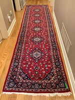 Full length view of runner laid on hardwood floor showing red field and central medallion pattern