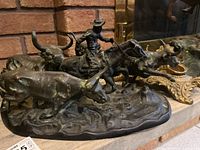 Overall view of bronze patinated metal sculpture of a cowboy herding cattle on oval base