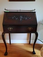 Front view of closed secretary desk showing carved foliate motif on drop-front and brass drawer pulls on dovetailed drawer.