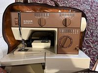 Singer Merritt 3014 sewing machine front view inside brown carrying bag showing control panel and stitch options.