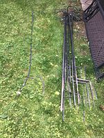 All nine metal shepherds hooks laid on grass and near outdoor furniture showing pointed ground stakes and various curved/ornamental hook tops.