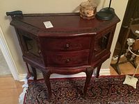 Front angle view of wooden side table showing two drawers, glass paneled side doors with carved trim and curved legs.