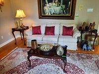 Photo capturing the wood side table with carved legs next to a cream upholstered couch, showcasing the classic style and polished finish.