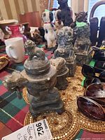 Photo showing front and side views of three stoneware incense burners with lion-dog lids and rings, placed on a patterned cloth with other decorative items in background.