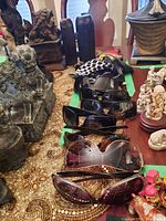 Photo showing 9 pairs of sunglasses arranged in a row on a decorated table with fabric cases behind them.