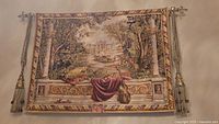 Front view of the woven decorative tapestry hung on the wall showing the ambient pastoral scene, tassel details and hanging rod.