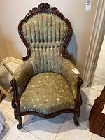 Front view of Victorian style armchair showing carved wood frame and floral fabric upholstery.