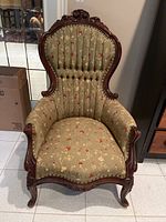Front view of Victorian style wooden and fabric armchair showing carved wooden backrest and floral upholstery