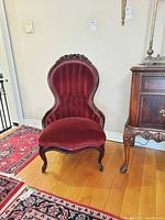 Front view of the Victorian chair showing tufted velvet back, carved wood top crest, and curved legs on hardwood floor with rugs.