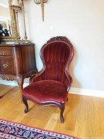 Front view of Victorian chair showing carved wood top rail and red velvet upholstery with tufted backrest and curved seat.