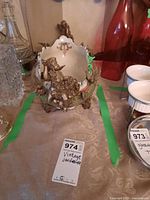 Front view showing overall jardiniere with cherub handle, bowl and base with floral and vine bronze-tone detail, alongside adjacent glass decanters and cups.