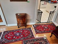 Two wool rugs on wooden floor, showing red floral designs and white tassels; one smaller rug placed atop the other.