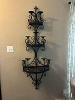 Front view of black wrought iron three-tier wall-mounted candle holder with intricate scrollwork design.