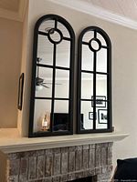 Two black framed arched mirrors hung side by side above a brick fireplace with clear reflections and visible grid pattern dividing the mirrors.