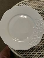 White ceramic plate showing decorative embossed floral pattern and scalloped edges.