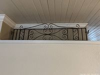 Black iron gate topper with delicate French scroll design mounted above interior wall opening.