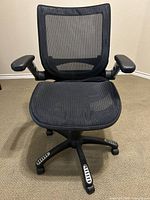 Front view of the black mesh ergonomic office chair showing the seat, adjustable armrests, and swivel five-star base with rolling casters.