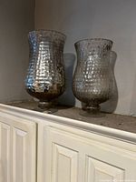 Pair of decorative mercury glass effect vases with textured checkerboard pattern displayed on top of a white cabinet.