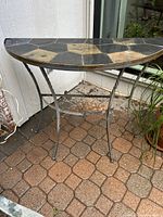 Side view of the half-moon shaped table showing metal legs and slate tile top with black and tan geometric pattern.