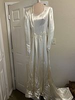 Full front view of ivory satin 1940s wedding dress on mannequin showing long sleeves and smooth flowing skirt.