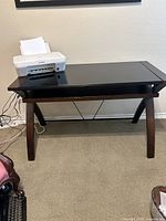 Desk with black glass top and wooden frame supporting a Canon printer on top, showing overall desk structure and placement of items.