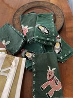 Green fabric table napkins with embroidered Christmas-themed designs including reindeer and other festive motifs.