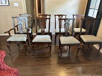 Full view of set of eight traditional wooden dining chairs on hardwood floor in room with beige walls and door in background.