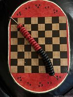 Top view of Checkerboard painted with watermelon design, featuring red and black checker pieces on cord.
