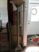 Full view of the torchiere floor lamp showing its tall structure next to stacked boxes and a door.
