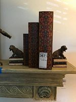 Wide view of dog bookends holding three ornate book-shaped storage boxes, on a decorative shelf.