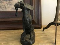 Close-up of metal dog figurine holding a bird in its mouth with detailed texture.