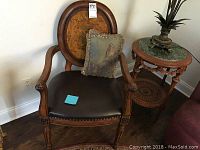 Front view of wooden armchair with burl wood backrest, dark leather seat with brass nail trim, and carved arms. Throw pillow visible on seat.