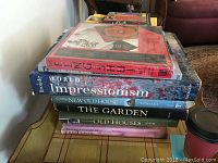 Stack of books on a wooden surface with visible titles 'World of Impressionism', 'Creating New Old House', 'The Garden', and 'Old Houses'. Top books have colorful covers with art themes.