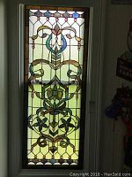 Full view of rectangular stained glass panel with floral scroll design and cabochons