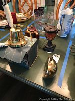 Brass nautical bell in original box, brass apple halves, ceramic teapot, glass bowls and goblets, metal urn vase, white ceramic figurine on table