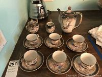 Full set arranged on table with coffee pot, sugar bowl, creamer, six cups and saucers featuring dragon motifs and gold detailing.