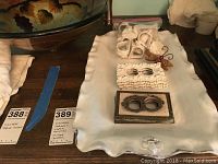 Photo showing assorted ceramic napkin holders and metal outlet covers placed on a white cloth with decorative edges.